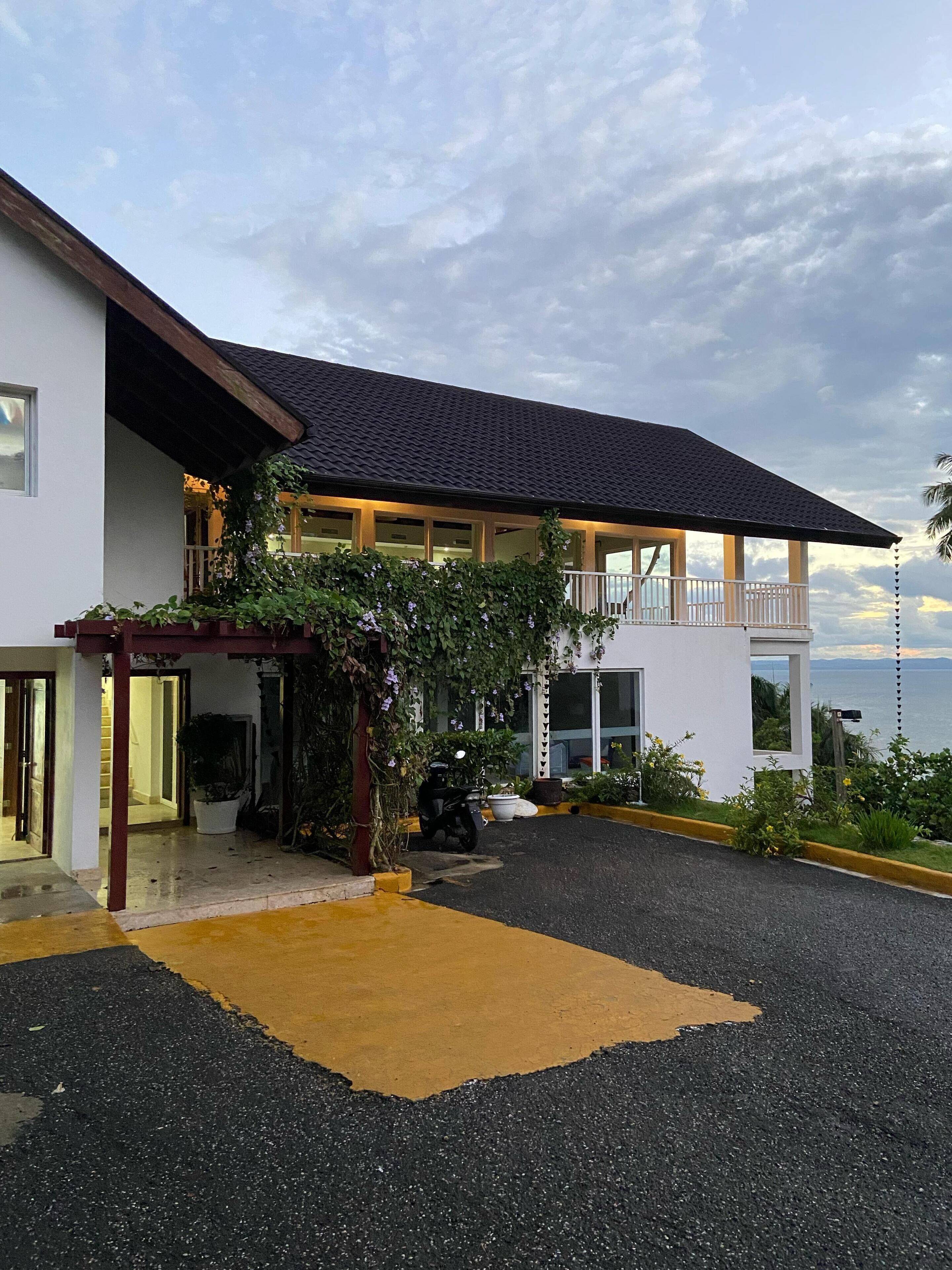 Ein modernes, zweistöckiges Haus mit überdachter Veranda, befestigter Auffahrt und Meerblick.
