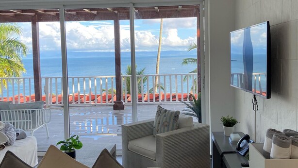 A modern living room with a large window overlooking a pool and ocean view. - APARTAMENTO VISTA MARE 9-202 (Samana)