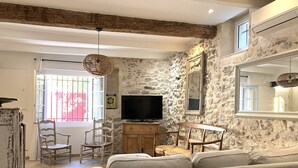 Une pièce rustique avec des murs en pierre, un plafond en bois, un canapé, une télévision et un coin repas avec des chaises.