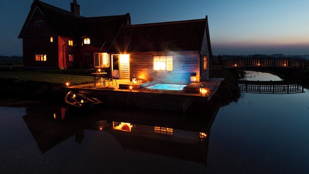Una cabaña junto al lago con jacuzzi, un muelle y un puente de madera al fondo.