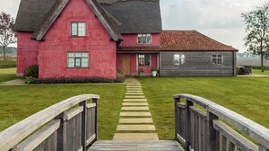 Una casa con fachada roja, techo gris y una terraza de madera que conduce a la puerta principal.