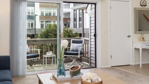 A modern living room with a large window, a wooden coffee table, and a blue sofa. - Newly Furnished Sun Drenched Duplex Private Deck Steps to the Beach & Boardwalk! (Seaside Heights)