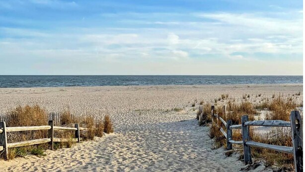A sandy beach with wooden fences and a clear view of the ocean. - Newly Furnished Sun Drenched Duplex Private Deck Steps to the Beach & Boardwalk! (Seaside Heights)
