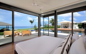 A modern bedroom with a large bed, a ceiling fan, and a view of the ocean and pool area. - Luxe Vacay Beachfront Sava Villa 2 | Villa Amarelo | Chef & Staff | LTH-13 (Phuket)