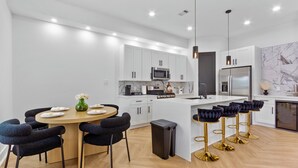 A modern kitchen with white cabinets, a central island with bar stools, and a dining area with a round table and chairs.