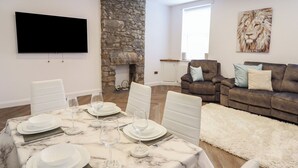 Un soggiorno moderno con camino in pietra, TV a schermo piatto montata a parete, divano marrone con cuscini e tavolo da pranzo bianco per quattro persone.