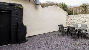 Un'area patio con tavolo e sedie, una porta nera e un muro in pietra.