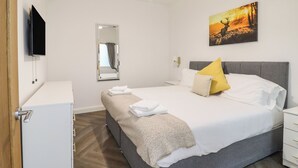 Una camera d'albergo con un letto, un comodino, uno specchio, una TV e un quadro appeso al muro.
