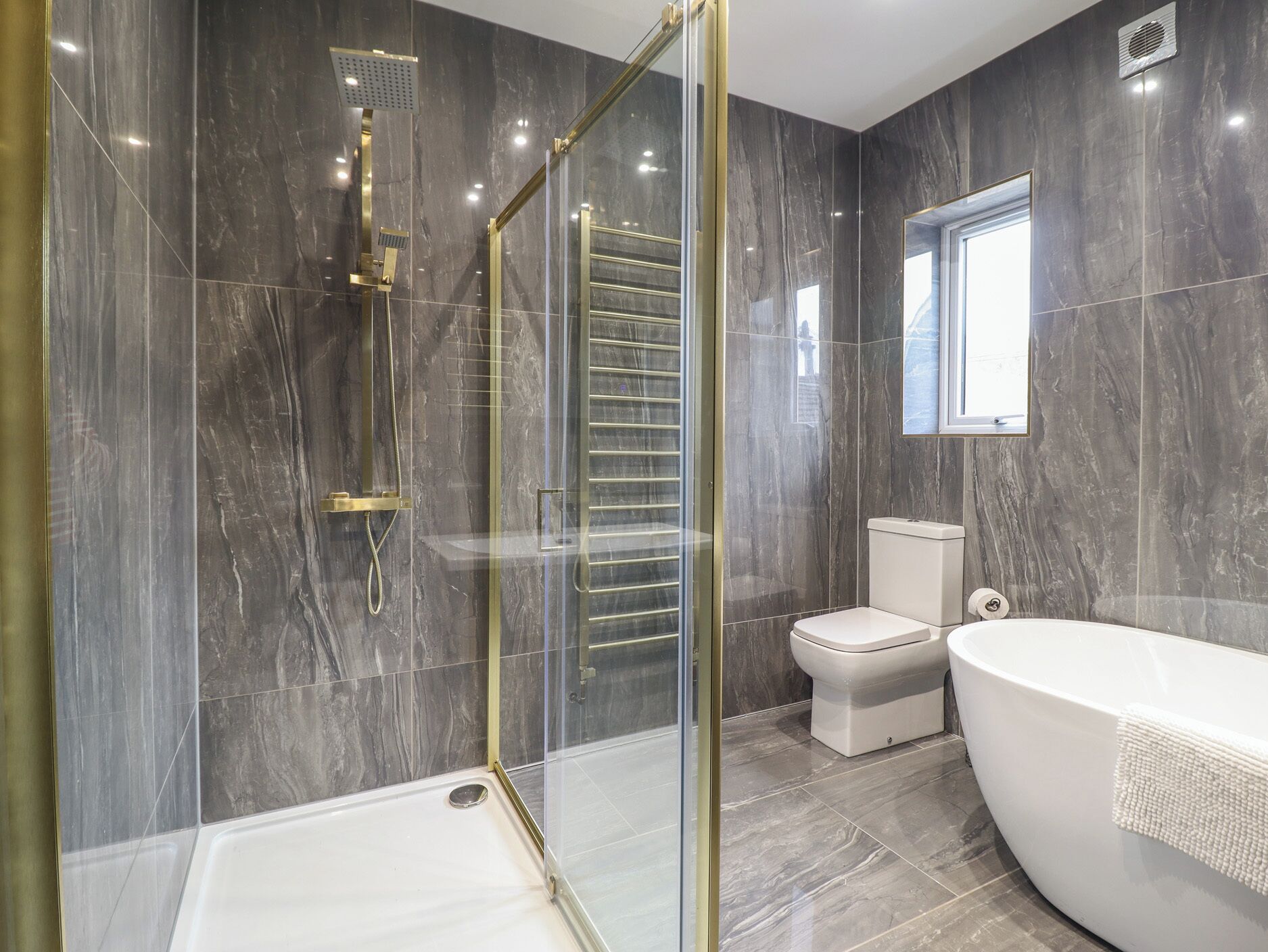 Un baño moderno con ducha envuelta en vidrio, una bañera independiente y un inodoro.