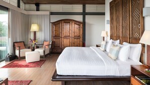A spacious bedroom with a large bed, a wooden wardrobe, a seating area with a chair and table, and a view through the window. - Luxe Vacay Beachfront Sava Villa 5 | Villa Malee Sai | Chef & Staff | LTH-16 (Takua Thung)