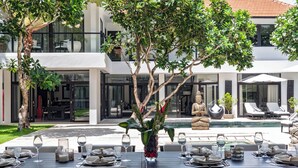 A dining area with tables set for a meal, a statue, and a pool in the background. - Luxevacay Anaya Manis Villa lvid3 (Badung)