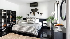 A modern bedroom with a black and white striped bedspread, a large mirror, and a wall-mounted elephant head sculpture. - Luxevacay Anaya Manis Villa lvid3 (Badung)