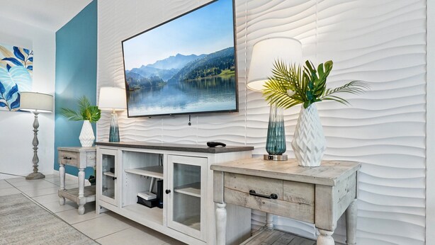 A modern living room with a large flat-screen TV mounted on a textured wall, a wooden console table with built-in shelves, and decorative vases.