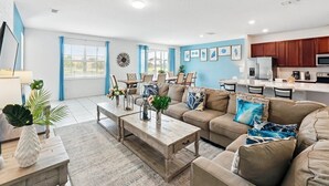A modern living room with a beige sofa, wooden coffee table, and a dining area with blue curtains.