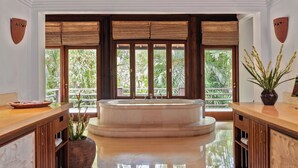 Ein geräumiges Badezimmer mit einer freistehenden Badewanne, Holzschränken und großen Fenstern mit Blick auf üppiges Grün.