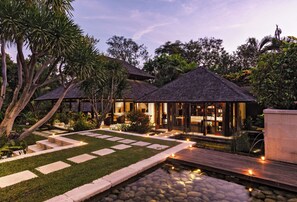 Un resort con varias construcciones de techo de paja, un jardín cuidado con un sendero de piedra y una pequeña fuente de agua.