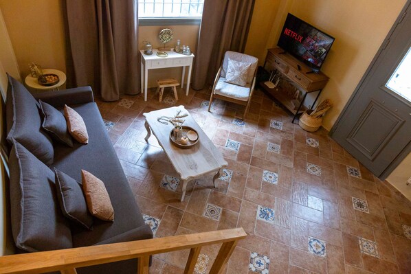 A living room with a sofa, a small table, a chair, and a television displaying 'NETFLIX'. - Strofilia Guest House (Markopoulo Mesogaias)