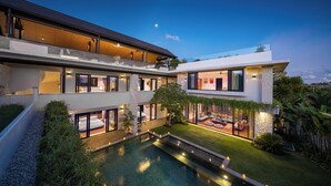 Una casa moderna de varios pisos con piscina, balcones y zonas de estar al aire libre.