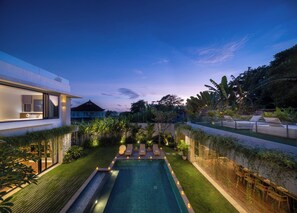 Una casa moderna con piscina, mobiliario de exterior y abundante vegetación.