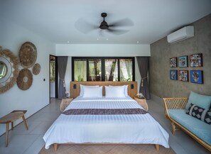 Un dormitorio amplio con una cama grande, un ventilador de techo y vistas a zonas verdes a través de las ventanas.