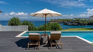 Un área junto a la piscina con dos sillones de mimbre, una mesa y una sombrilla.