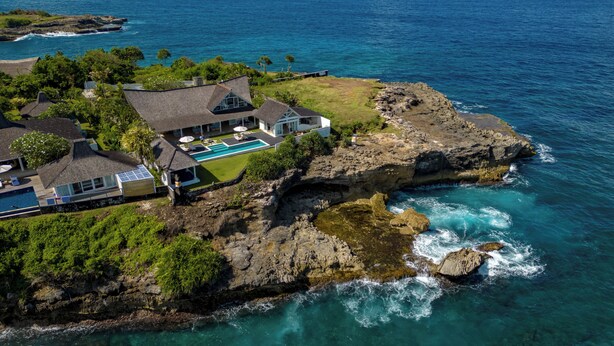 Una propiedad costera con una casa grande, piscina y costa rocosa.