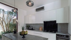 A modern kitchen with white cabinets, a granite countertop, a black stove, and a large window with plants. - Luxe Vacay Amara Pradi Chef and Staff included  lvid5 (Seminyak)