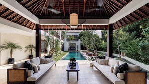 A spacious outdoor lounge area with a pool, two sofas, a coffee table, and potted plants. - Luxe Vacay Amara Pradi Chef and Staff included  lvid5 (Seminyak)