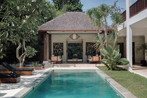 A swimming pool with lounge chairs, a covered seating area, and tropical plants.