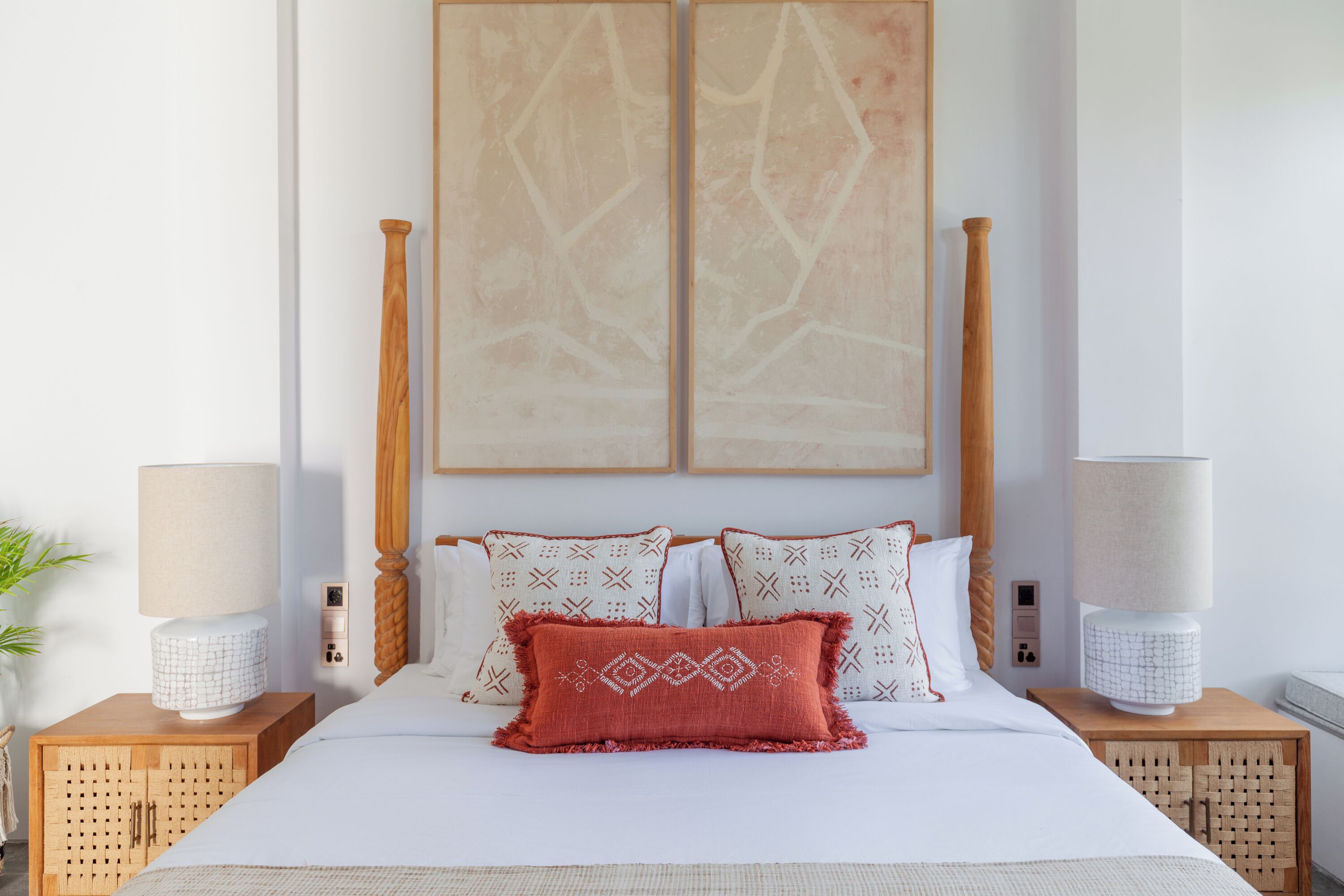 A neatly made bed with patterned pillows, a wooden headboard, and two bedside tables with lamps.