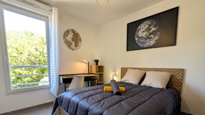 Un dormitorio con una cama, un escritorio, una silla, una obra de arte de un globo terráqueo y un cuadro enmarcado de la Tierra.
