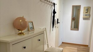Une pièce avec une commode blanche, un globe terrestre, un tableau encadré, une chaise, un porte-manteau avec un parapluie et un miroir au mur.
