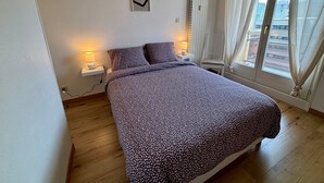 Une chambre à coucher avec un lit, deux lampes de chevet, une décoration en forme de cœur accrochée au mur et une fenêtre avec des rideaux.