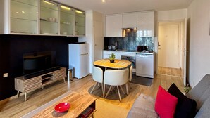 Un espace de vie compact comprenant un coin cuisine, un coin repas et un espace détente avec un téléviseur et un canapé.