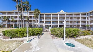 A multi-story hotel with a central courtyard, surrounded by palm trees and a well-maintained lawn.