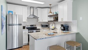 A modern kitchen with white cabinets, stainless steel appliances, a central island with bar stools, and a built-in microwave.