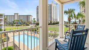 A balcony with a pool, palm trees, and high-rise buildings in the background.