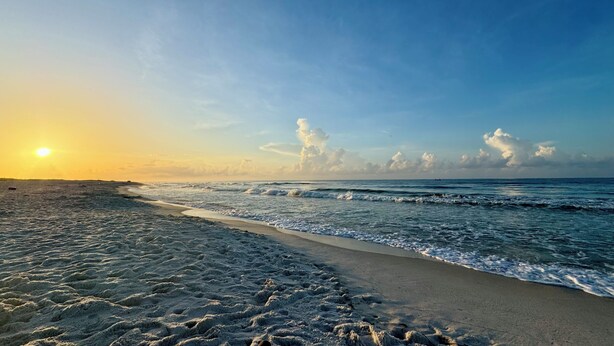 A beach with a clear sky and the sun setting on the horizon.