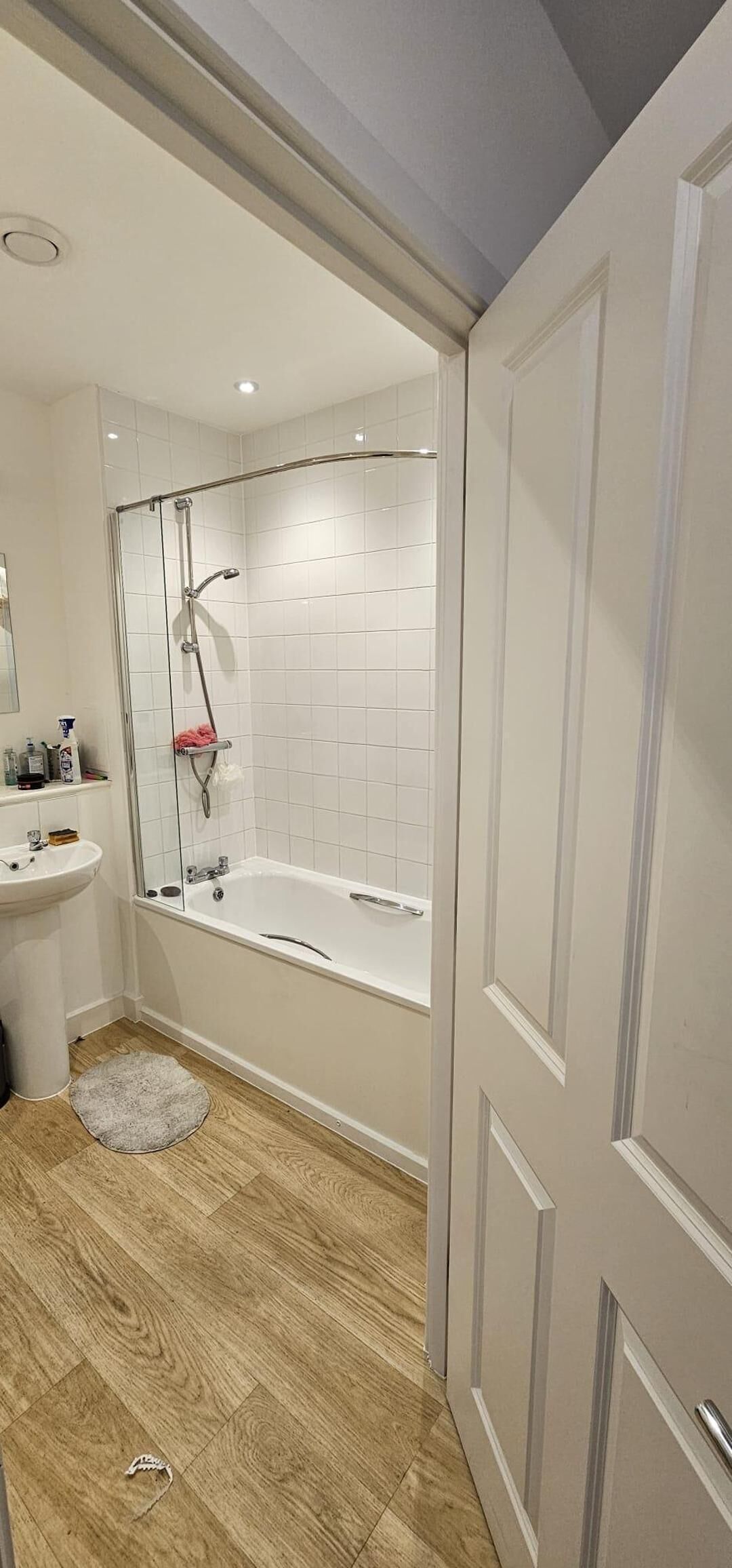 A bathroom with a glass-enclosed shower, a white sink, and a wooden floor.
