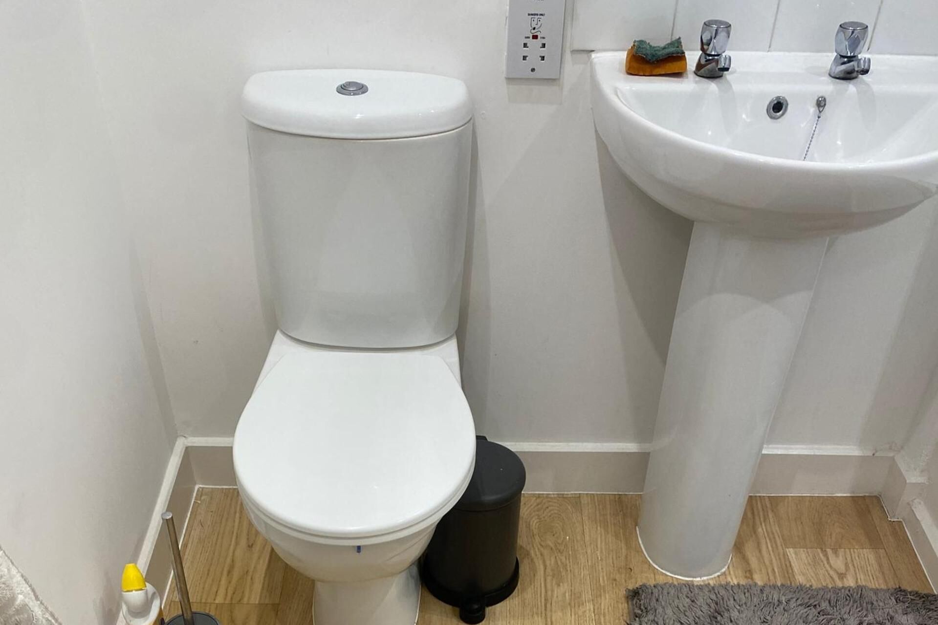 A bathroom with a white toilet, a sink, and a trash bin.