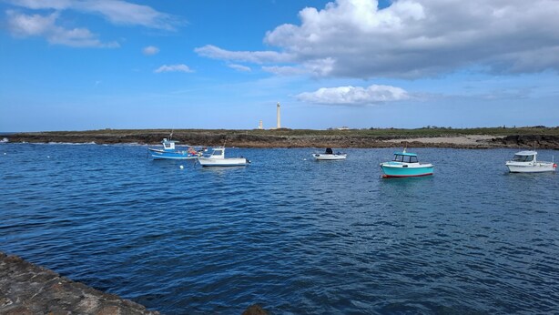 A coastal scene with several boats anchored near a rocky shore, a lighthouse in the background, and a clear sky. - Close to Barfleur, its port and beaches, courtyard for parking, bicycle shelter (Sainte-Geneviève)
