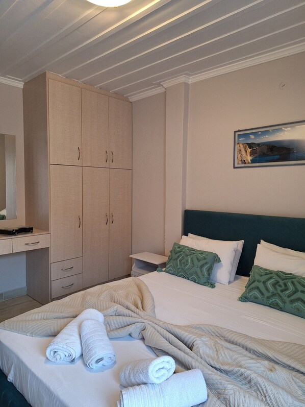 A hotel room with a bed, a large wardrobe, a desk, and a painting on the wall.