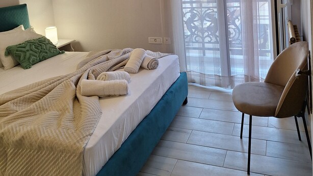 Une chambre d’hôtel avec un lit, une chaise, une fenêtre avec des rideaux et une vue sur les bâtiments environnants.
