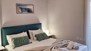 Un lit bien fait, avec une tête de lit de couleur turquoise, un plaid à motifs et des serviettes enroulées posées sur le bord.
