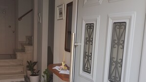 Un couloir doté d’un sol à carreaux, une porte blanche ornée de panneaux de verre décoratifs et un escalier menant à l’étage supérieur.