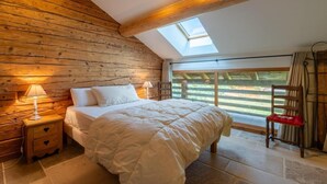 A bedroom with a sloped ceiling, wooden walls, a skylight, a bed with white bedding, a nightstand with a lamp, and a chair with a red cushion. - Wifi, 2nd floor, balcony, fireplace or stove, tv, ski locker, 85m², Le Grand Bornand (Le Grand-Bornand)
