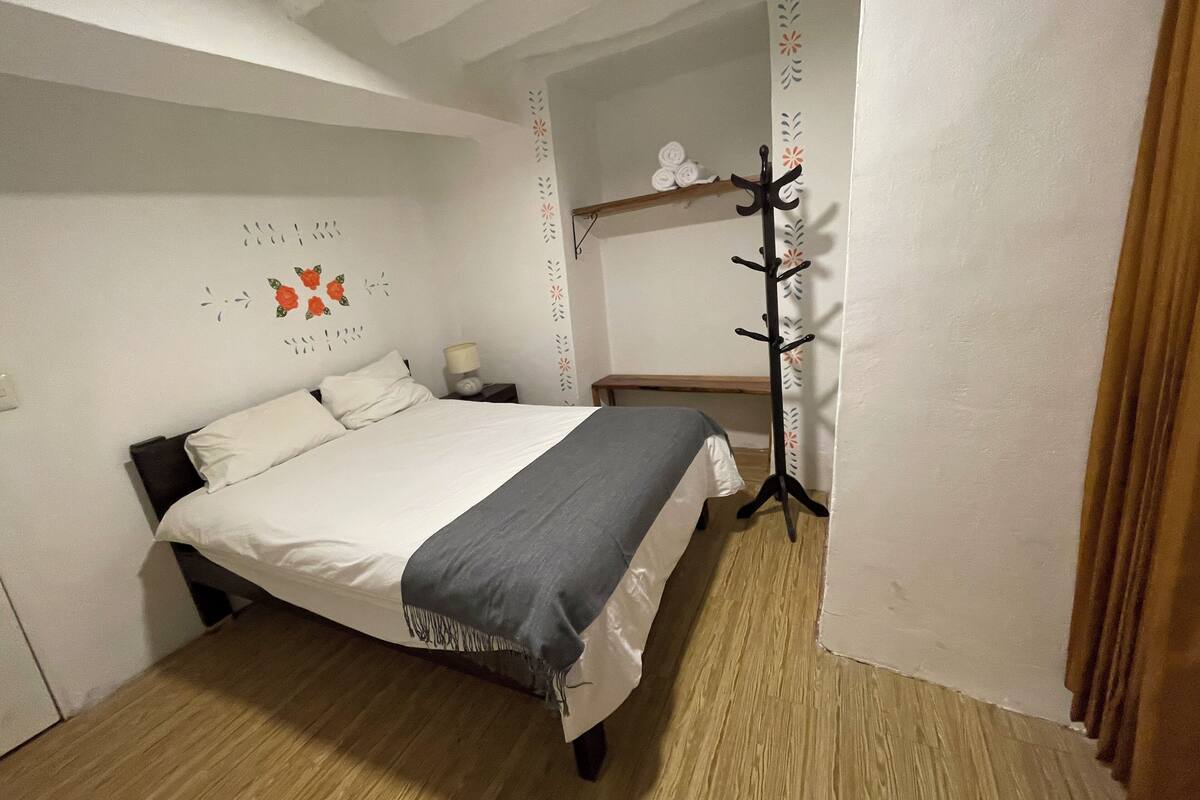 A bedroom with a bed, a nightstand, a lamp, a coat rack, and a wall with floral decals.