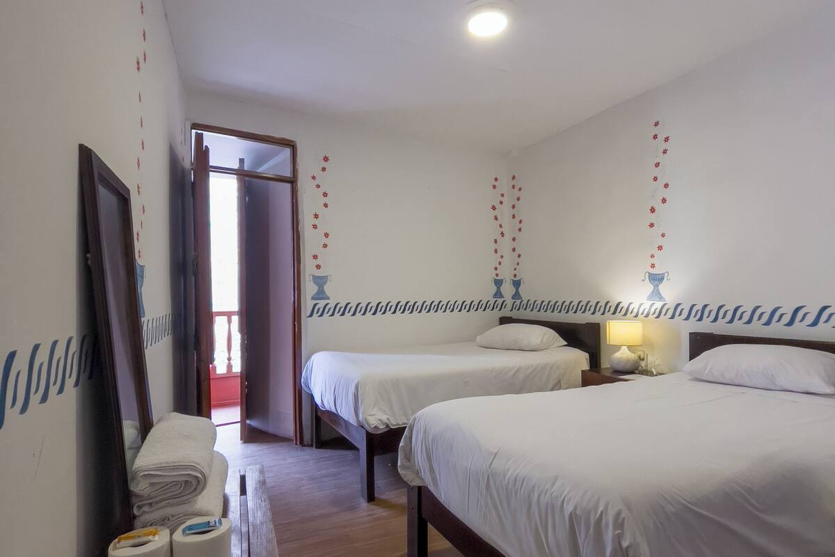 A hotel room with two single beds, a wooden floor, a table with toiletries, and a door leading to a balcony.
