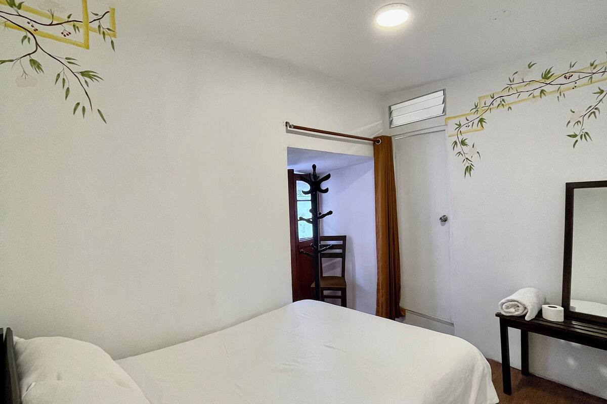 A hotel room with a bed, a wooden floor, a coat rack, and a mirror.
