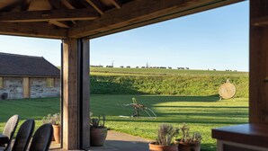 Ein überdachter Außenbereich mit Sitzgelegenheiten und Blick auf ein grünes Feld sowie ein Gebäude im Hintergrund.